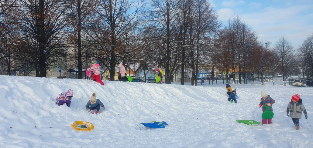 Na zdjęciu: Grupa przedszkolaków w kolorowych kombinezonach bawi się na śniegu