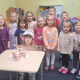Na zdjęciu grupa przedszkolaków wraz z solenizantką siedzącą przy stoliku z tortem