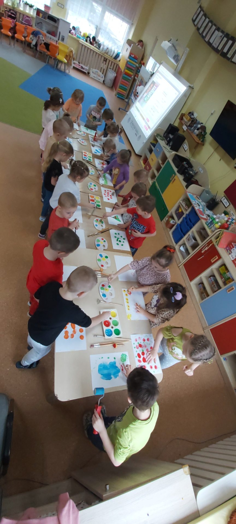 dzieci stojące wokół stolika, malują farbami