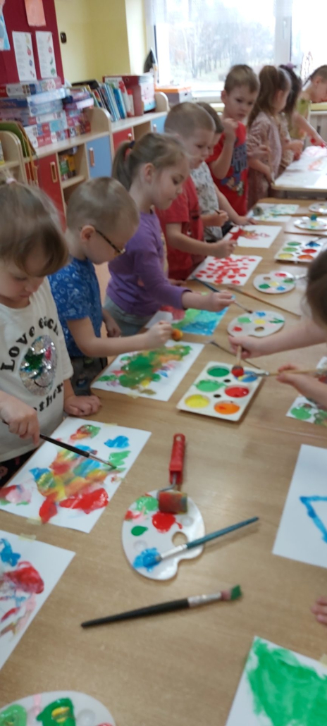 dzieci stojące wokół stolika, malują farbami