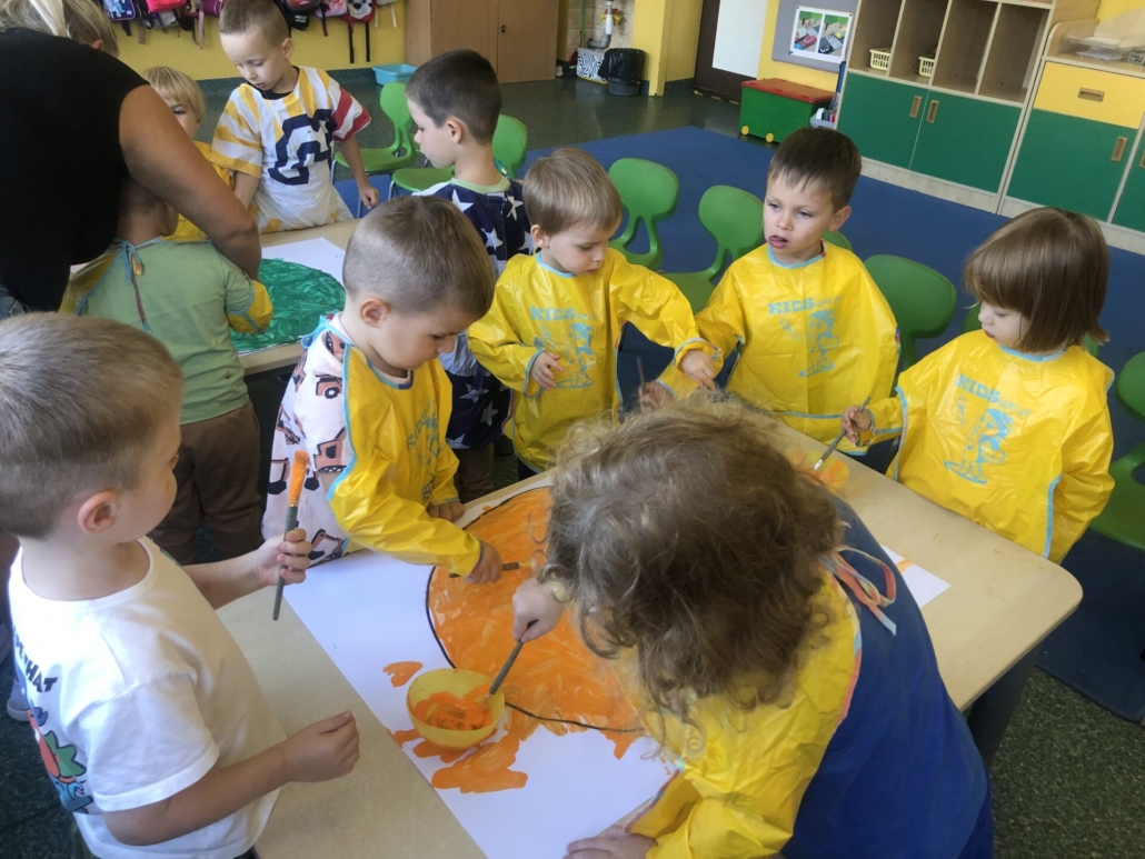 Grupa dzieci maluje koło na kolor pomarańczowy.