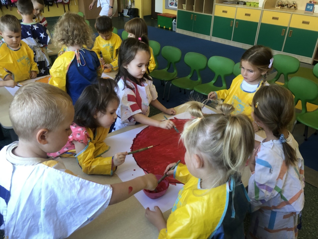 Grupa dzieci maluje koło na kolor czerwony.