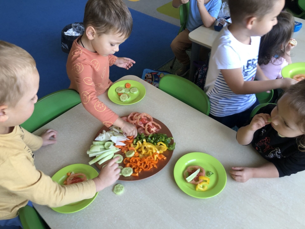 Dzieci częstują się pokrojonymi warzywami.